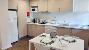 A modern kitchen with a refrigerator, microwave, toaster, sink, and a dining table set with plates and cutlery. - LEGACY SUITES & APARTMENTS ALBUFEIRA AL (Albufeira)