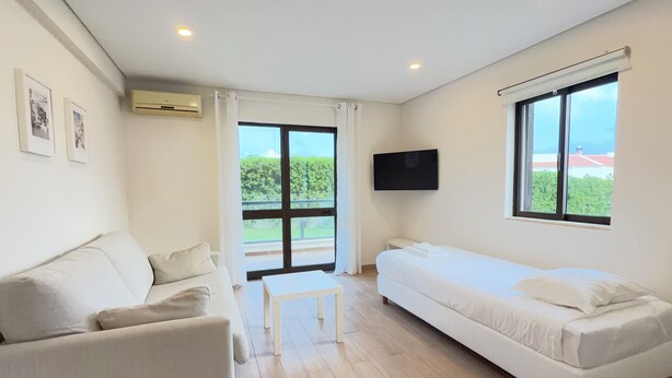 A room with a sofa, a bed, a TV, and a window with a view of greenery. - LEGACY SUITES & APARTMENTS ALBUFEIRA AL (Albufeira)