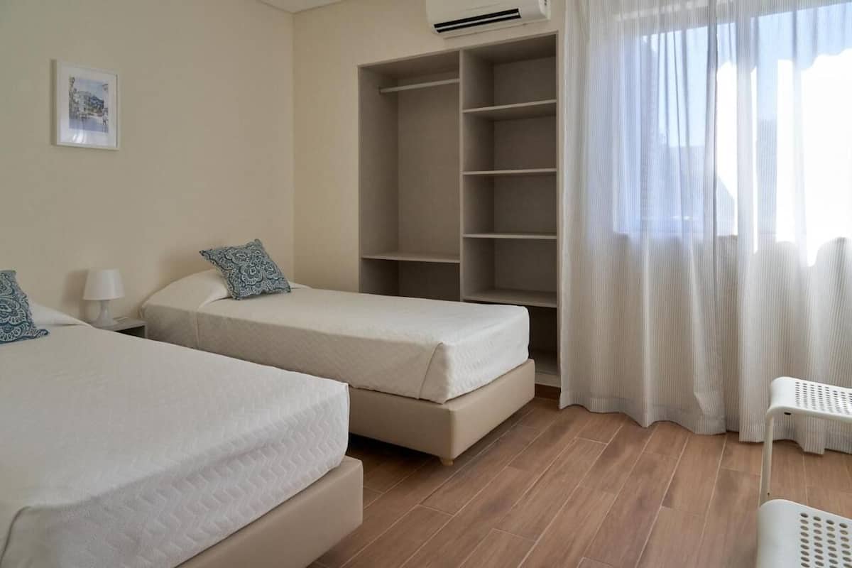 Une chambre avec deux lits, une armoire, une fenêtre avec des rideaux et un climatiseur fixé au mur.