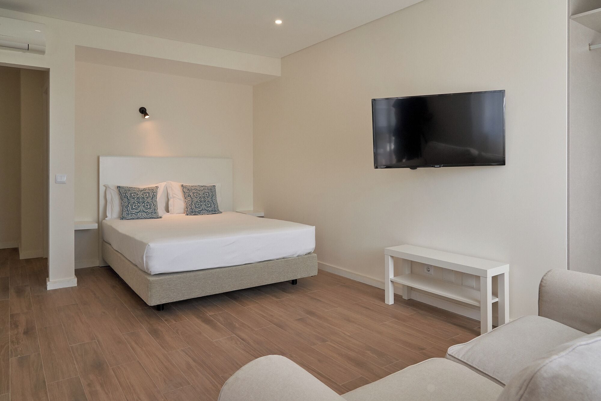 Una camera da letto moderna con un letto, una TV a parete e un piccolo tavolino bianco.