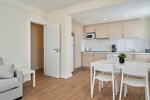 A modern kitchen with white cabinets, a microwave, a coffee maker, and a dining area with a table and chairs. - LEGACY SUITES & APARTMENTS ALBUFEIRA AL (Albufeira)