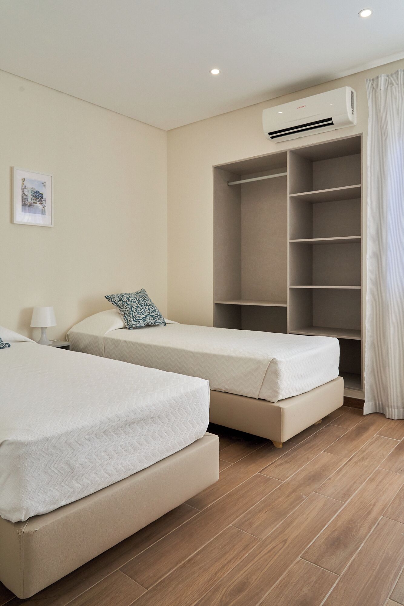 A hotel room with two beds, a wardrobe, an air conditioning unit, and a framed picture on the wall.