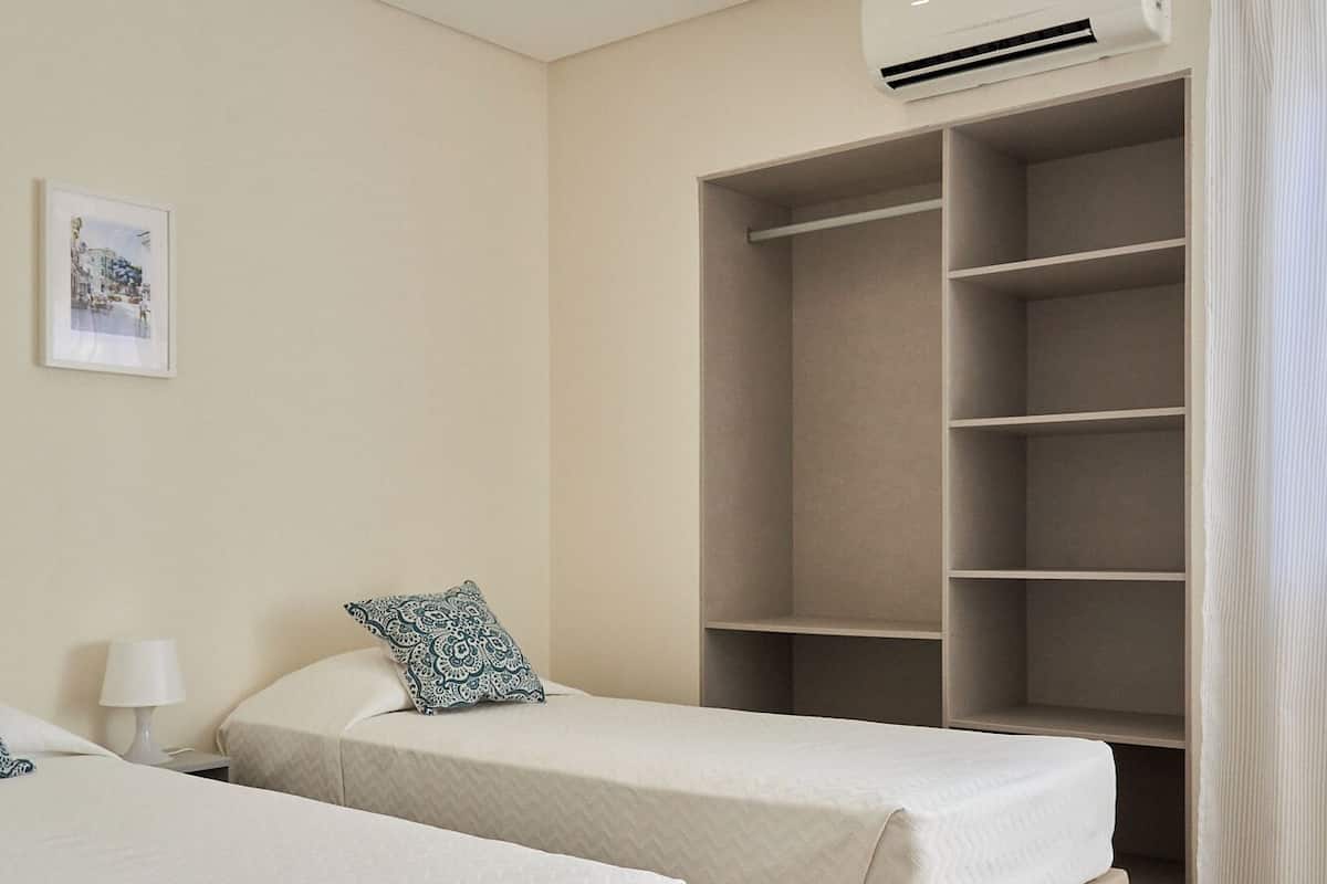 Habitación de hotel con dos camas, un armario, aire acondicionado y un cuadro en la pared.