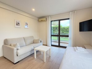 A hotel room with a sofa, a small table, a bed, a TV, and a sliding glass door to the outside. - LEGACY SUITES & APARTMENTS ALBUFEIRA AL (Albufeira)