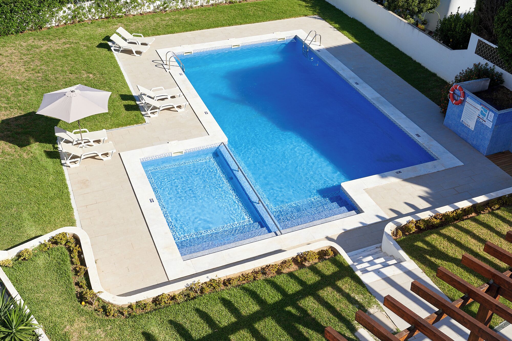 A rectangular pool with a small adjacent section, surrounded by a concrete deck and a grassy area with lounge chairs.