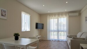 A modern living room with a white table, chairs, a sofa, and a TV mounted on the wall. - LEGACY SUITES & APARTMENTS ALBUFEIRA AL (Albufeira)
