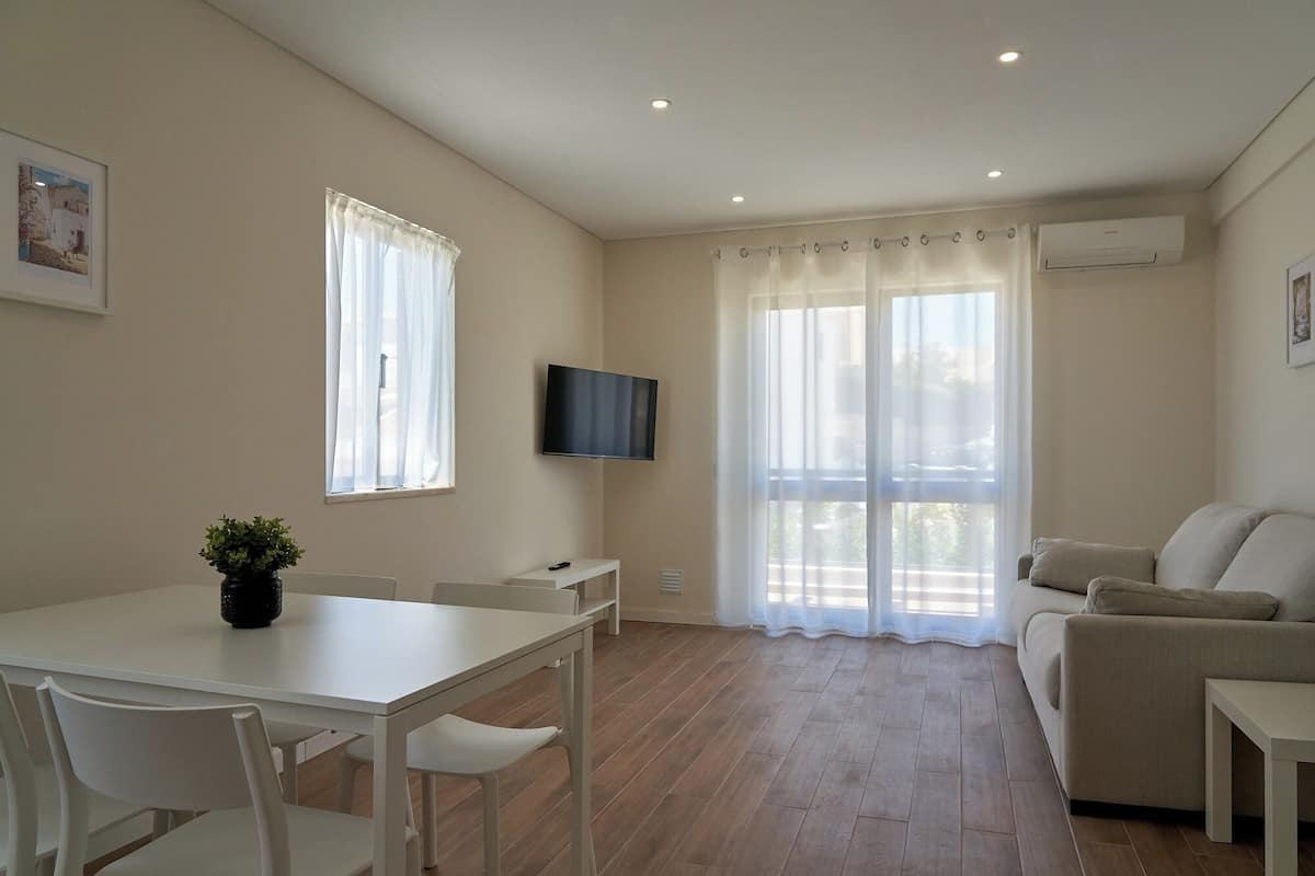 Un salon moderne avec une table blanche, des chaises, un canapé et un téléviseur fixé au mur.