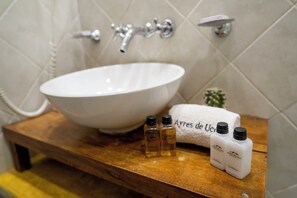Ein Badezimmer mit einem weißen Waschbecken, einem hölzernen Waschtisch und zwei Toilettenartikeln.