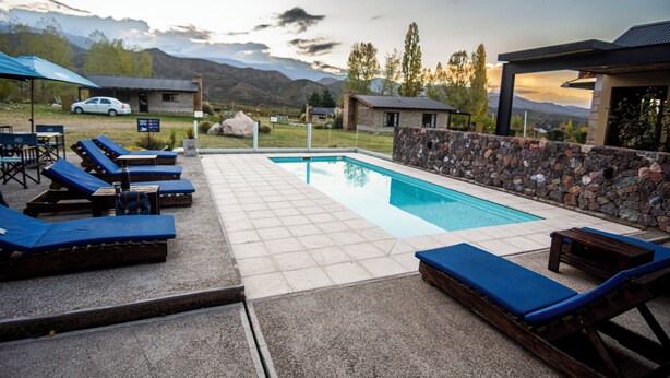A pool area with lounge chairs, a stone wall, and a view of mountains.