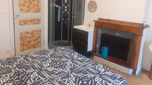 Une chambre avec une couvre-lit à motifs, une douche d’angle, un lavabo et une cheminée.