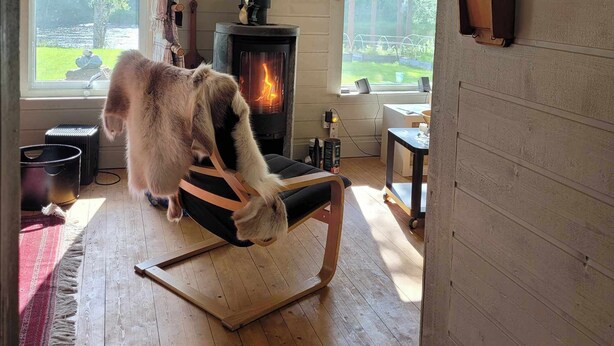 Une pièce chaleureuse avec un poêle à bois, un fauteuil et une vue sur l’extérieur.