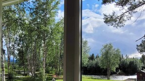 Une vue à travers une fenêtre sur un espace verdoyant, avec des arbres, une formation rocheuse et un petit bâtiment.