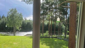 Une pièce dotée d’une grande fenêtre donnant sur un espace verdoyant, avec des arbres et une étendue d’eau.