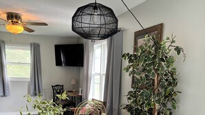 Uma mesa de madeira com luminária pendente trançada, uma planta em vaso e um leque decorativo.