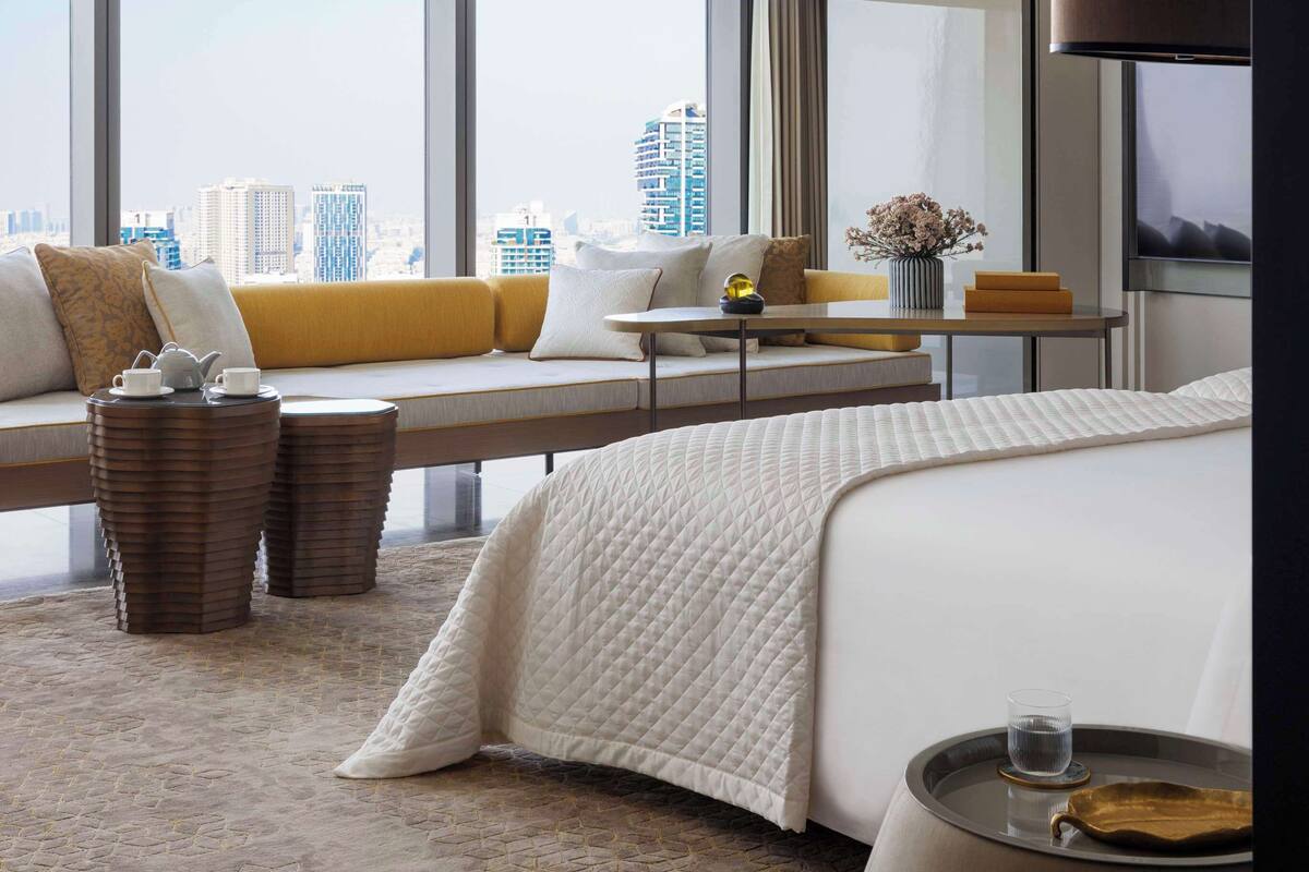 Une chambre d’hôtel moderne dotée d’une grande fenêtre, d’un canapé, d’un lit, d’une table de chevet et offrant une vue sur le paysage urbain.