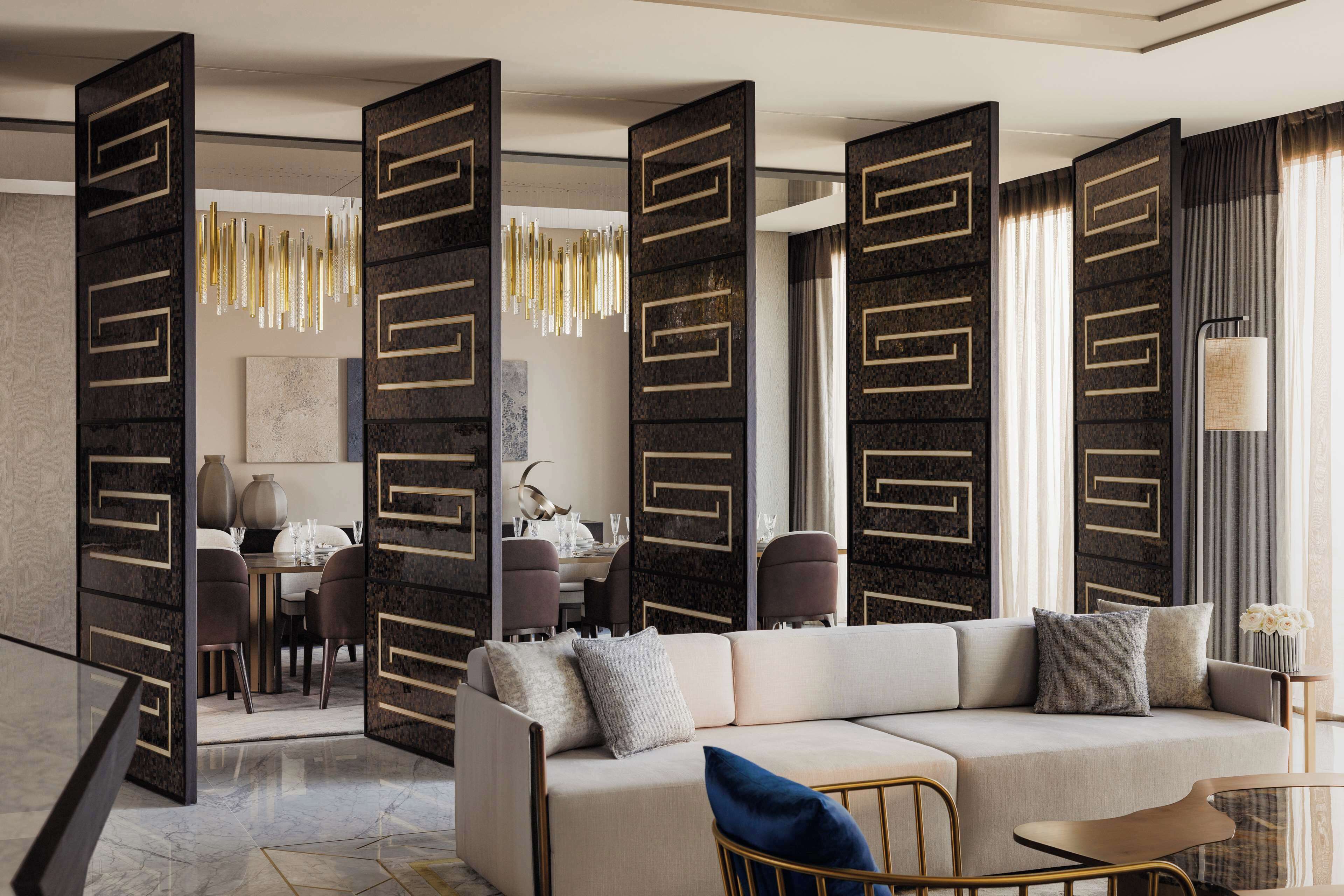 A modern living room with a beige sofa, a dining area with a table and chairs, and decorative wall panels.