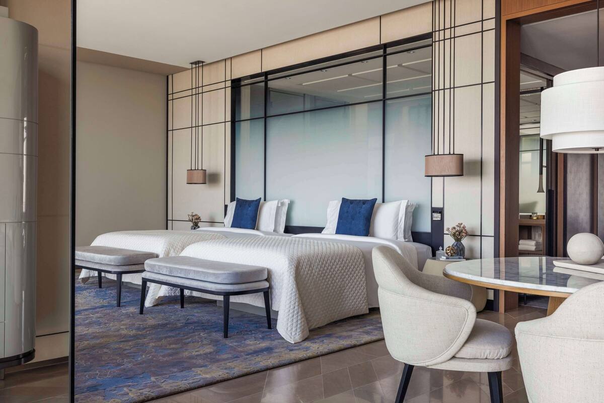 Une chambre d’hôtel moderne dotée d’un grand lit, d’un coin salon avec une table ronde et d’une cloison en verre.