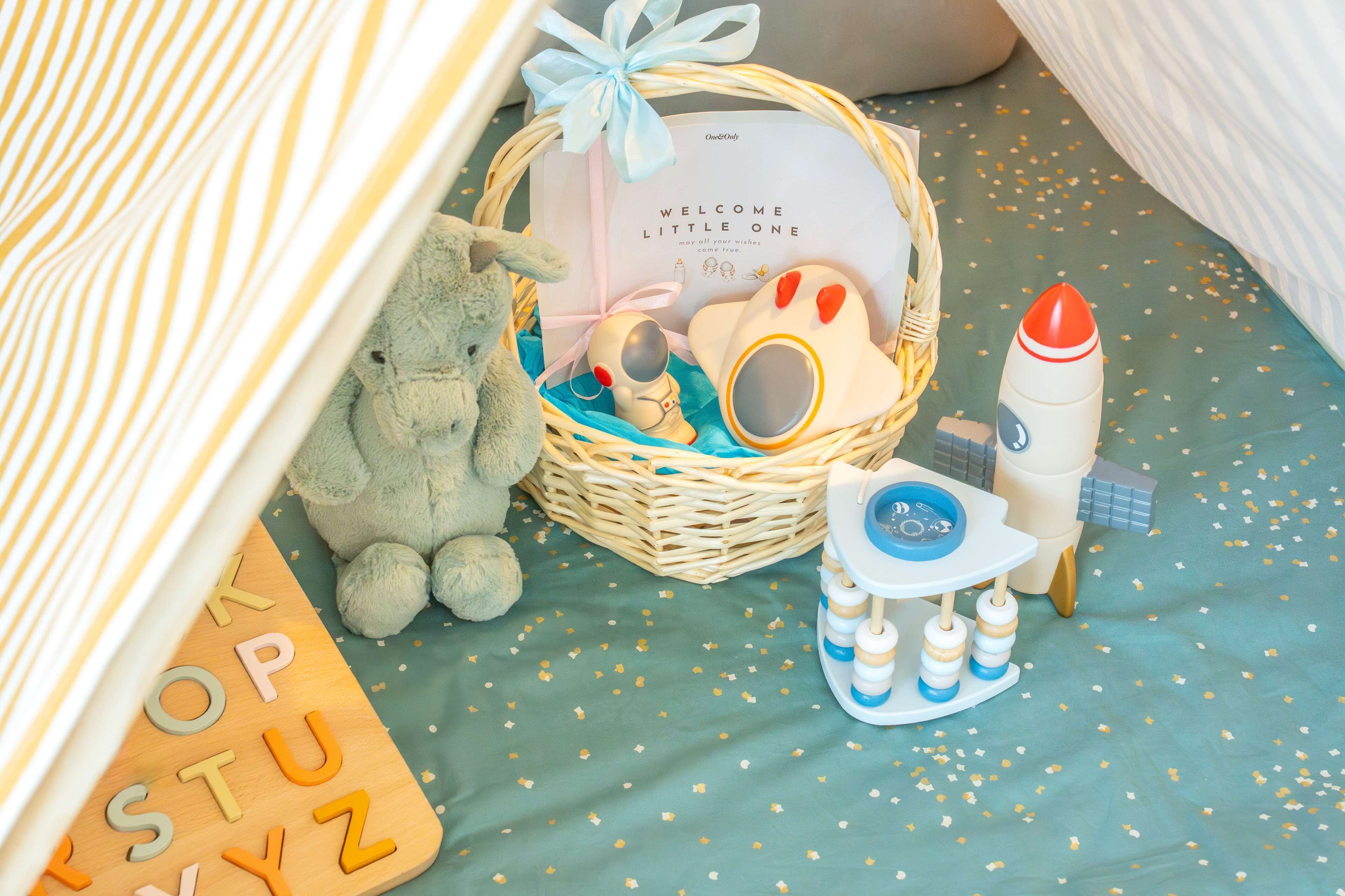 A cozy room with a bed, a stuffed toy, a basket with a welcome card, and a rocket toy.