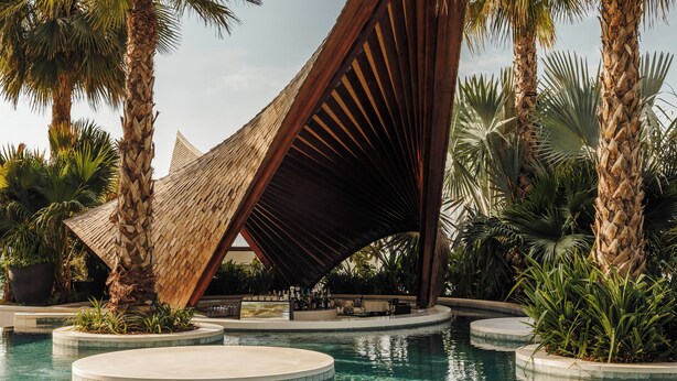 Un espace piscine doté d’une structure unique et moderne, entouré de palmiers et d’autres plantes tropicales.