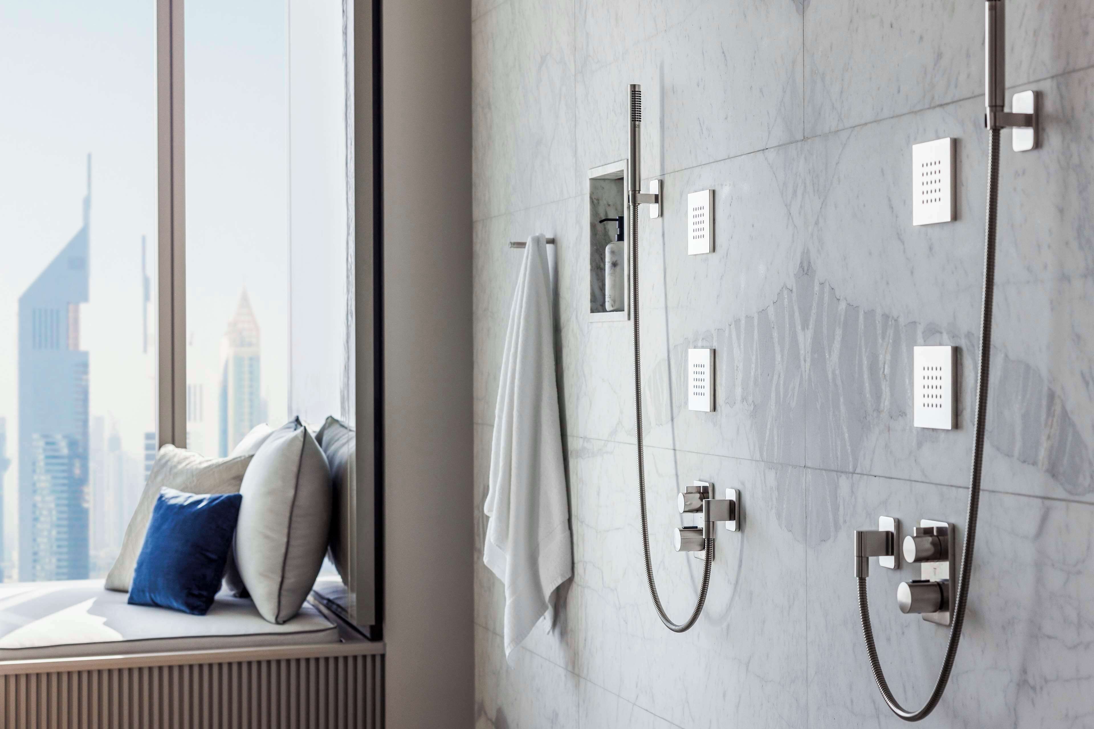Un baño moderno con ducha, toallero y vistas a un paisaje urbano a través de una ventana.