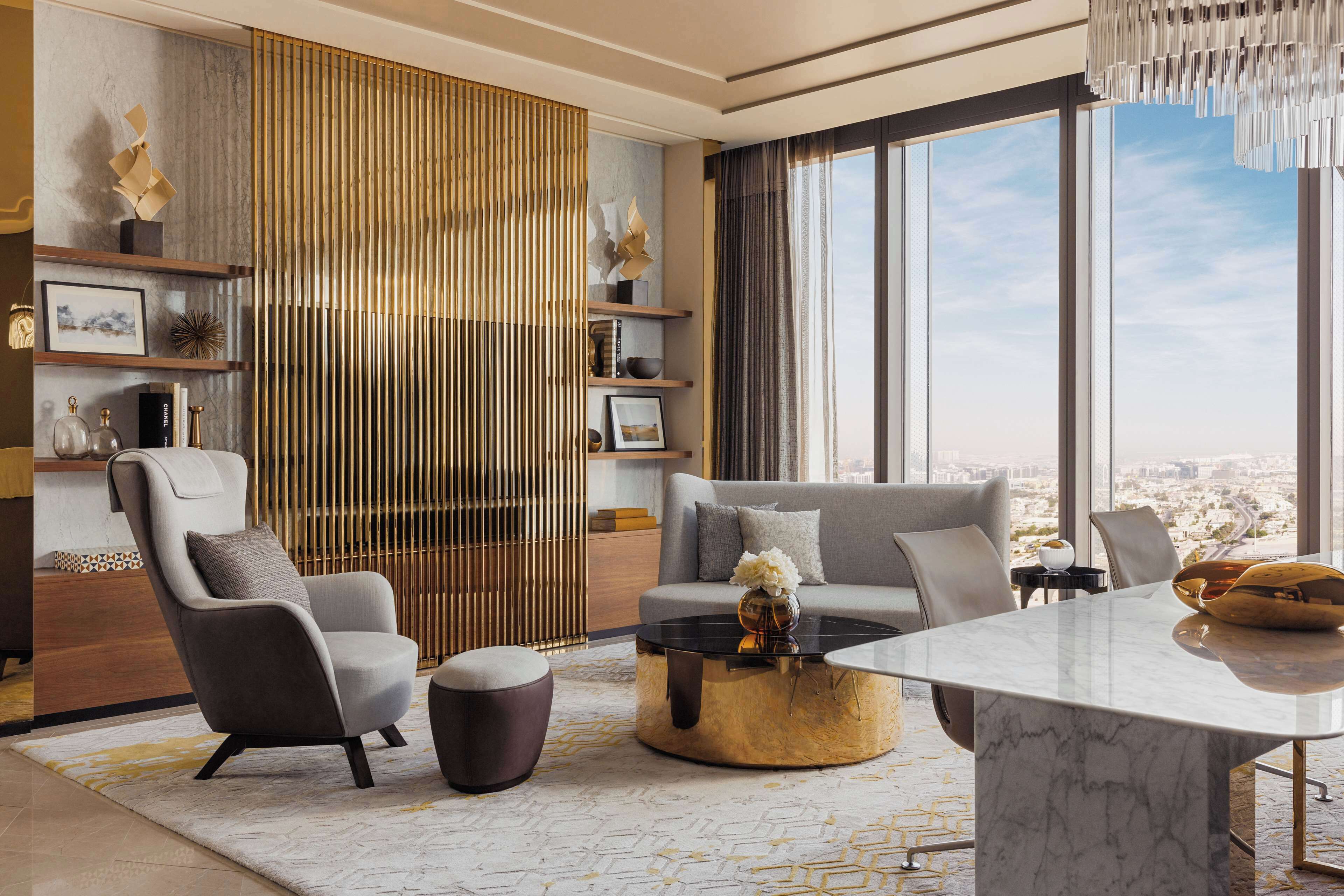 A modern living room with a sofa, armchair, coffee table, and a view of the city through large windows.