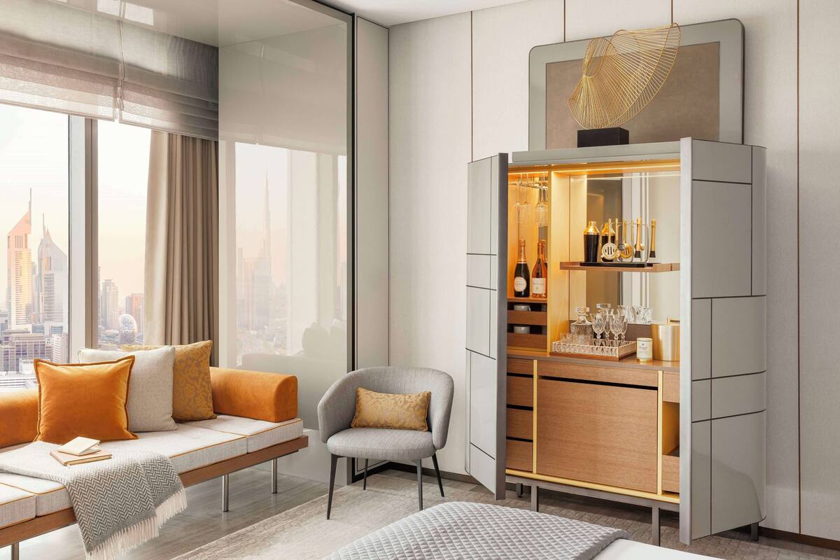Une chambre d’hôtel moderne avec vue sur la ville, un canapé avec des coussins, un fauteuil, un minibar et une grande fenêtre.