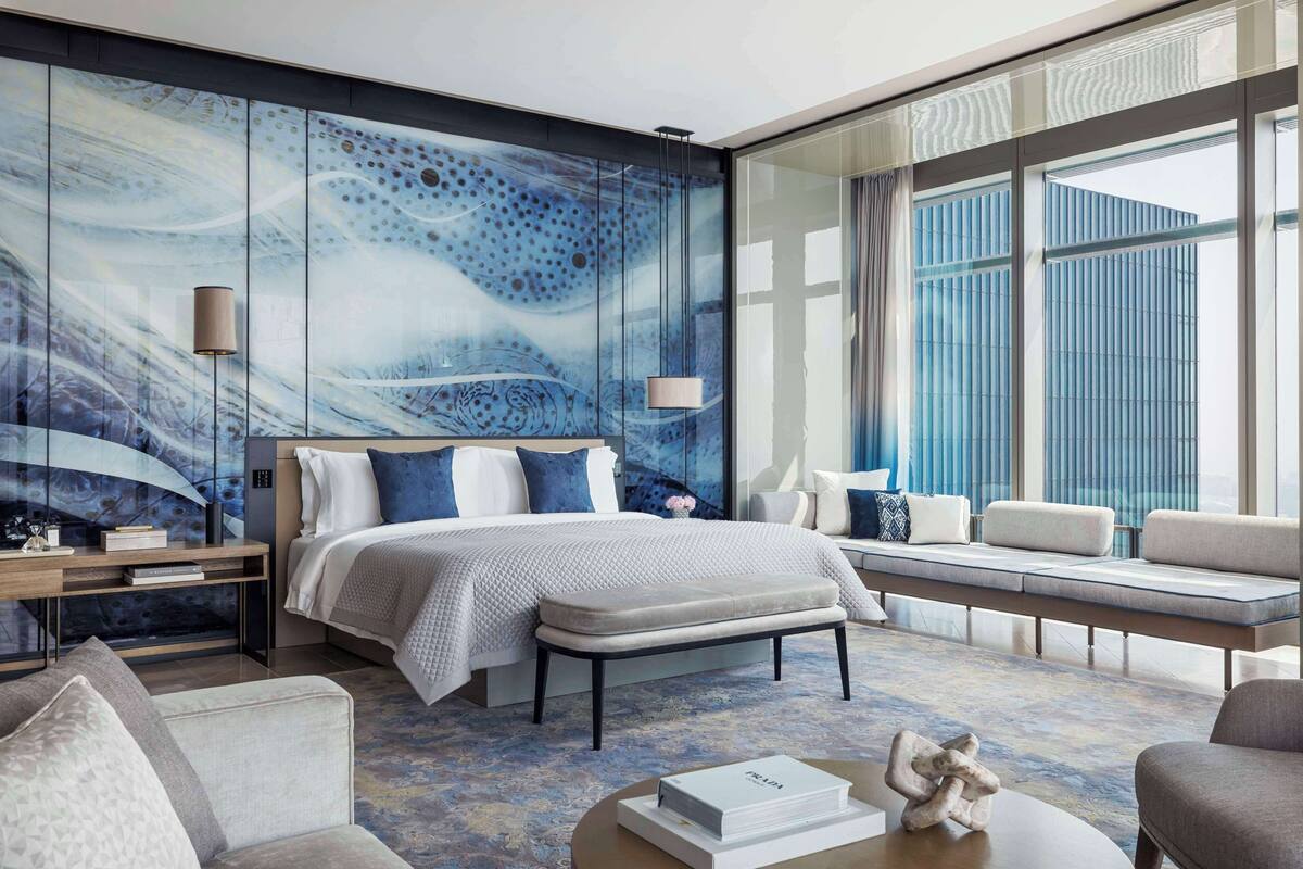 Une chambre d’hôtel moderne dotée d’un grand lit, d’un coin salon avec des canapés, d’une table basse et d’une grande fenêtre avec des rideaux.