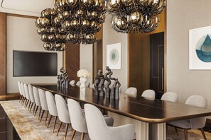 A conference room with a long table, white chairs, a large chandelier, and artwork on the walls.