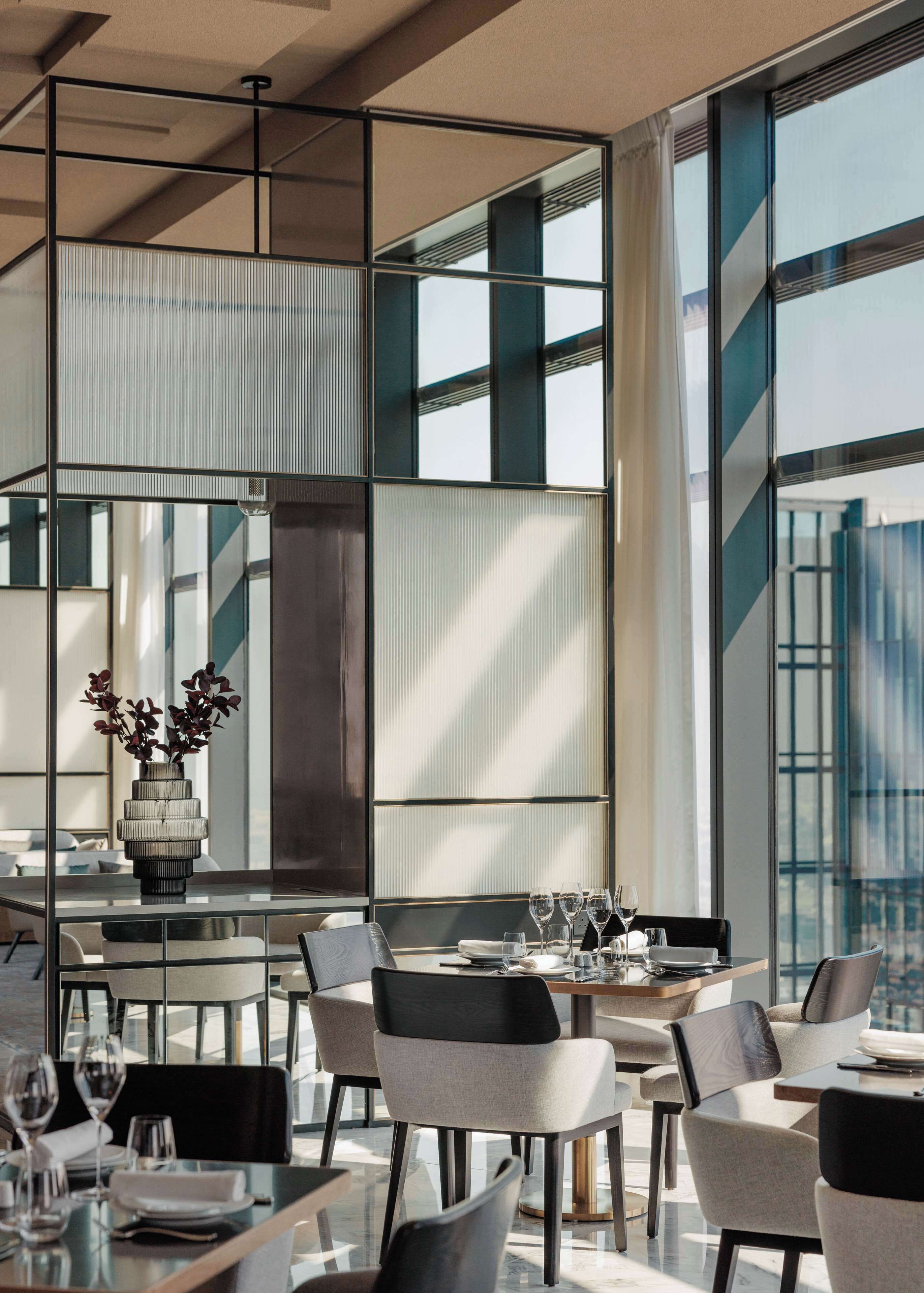 Un espace repas moderne avec une cloison en verre, un vase rempli de fleurs et une table dressée pour quatre personnes.