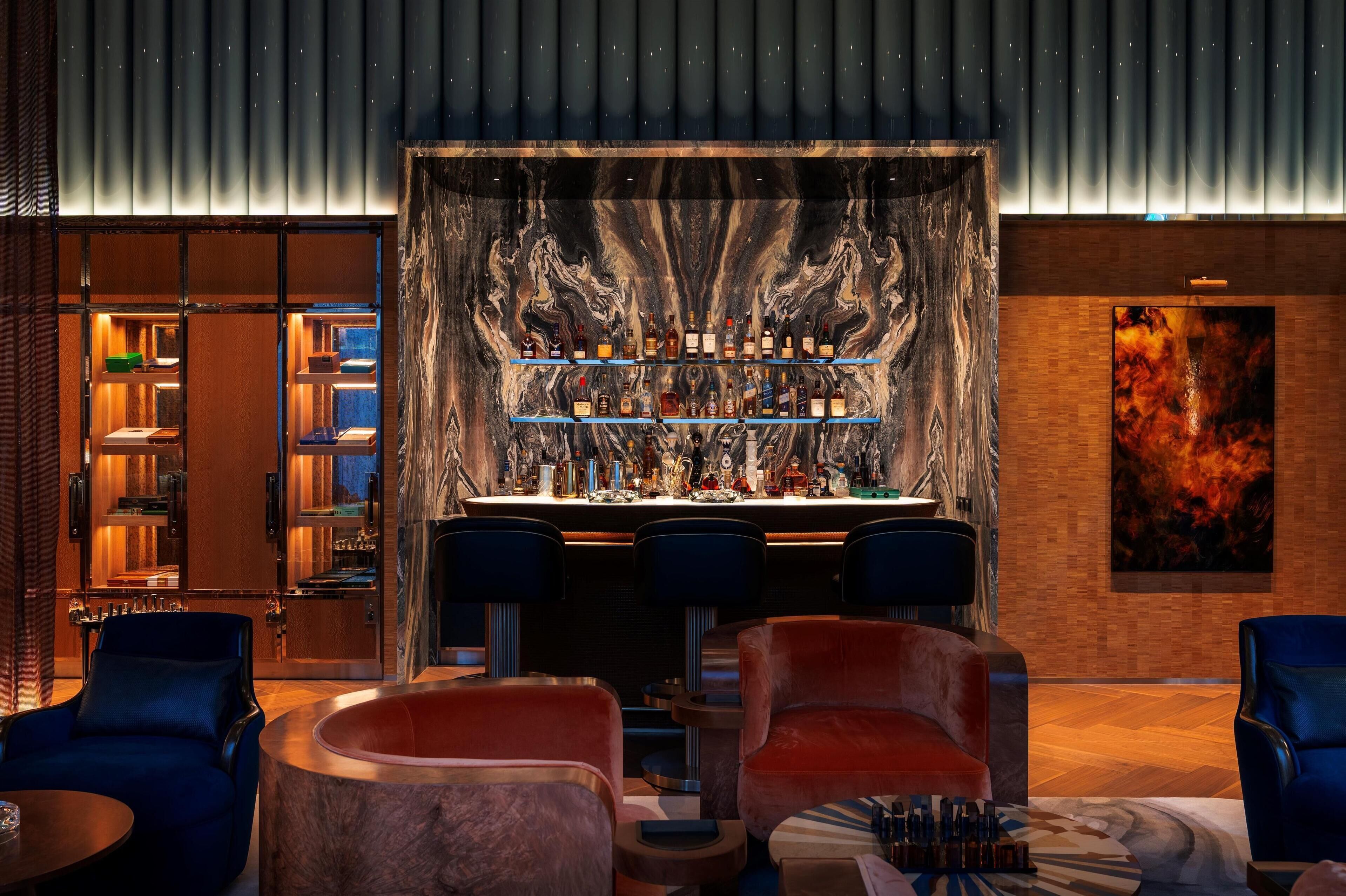 A bar area with a marble wall, shelves with bottles, and seating with a fire feature.