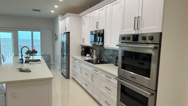 A modern kitchen with white cabinets, stainless steel appliances, and a large island with a sink. - Breathtaking sunrises from your balcony at this 3 bedroom, 2 bath home (Big Pine Key)