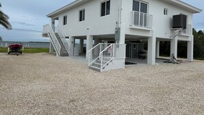 A two-story building with a covered outdoor area, a staircase, and a view of the water. - Breathtaking sunrises from your balcony at this 3 bedroom, 2 bath home (Big Pine Key)