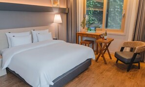 Een hotelkamer met een groot bed, een bureau met een computer, een stoel en een raam met uitzicht op bomen.
