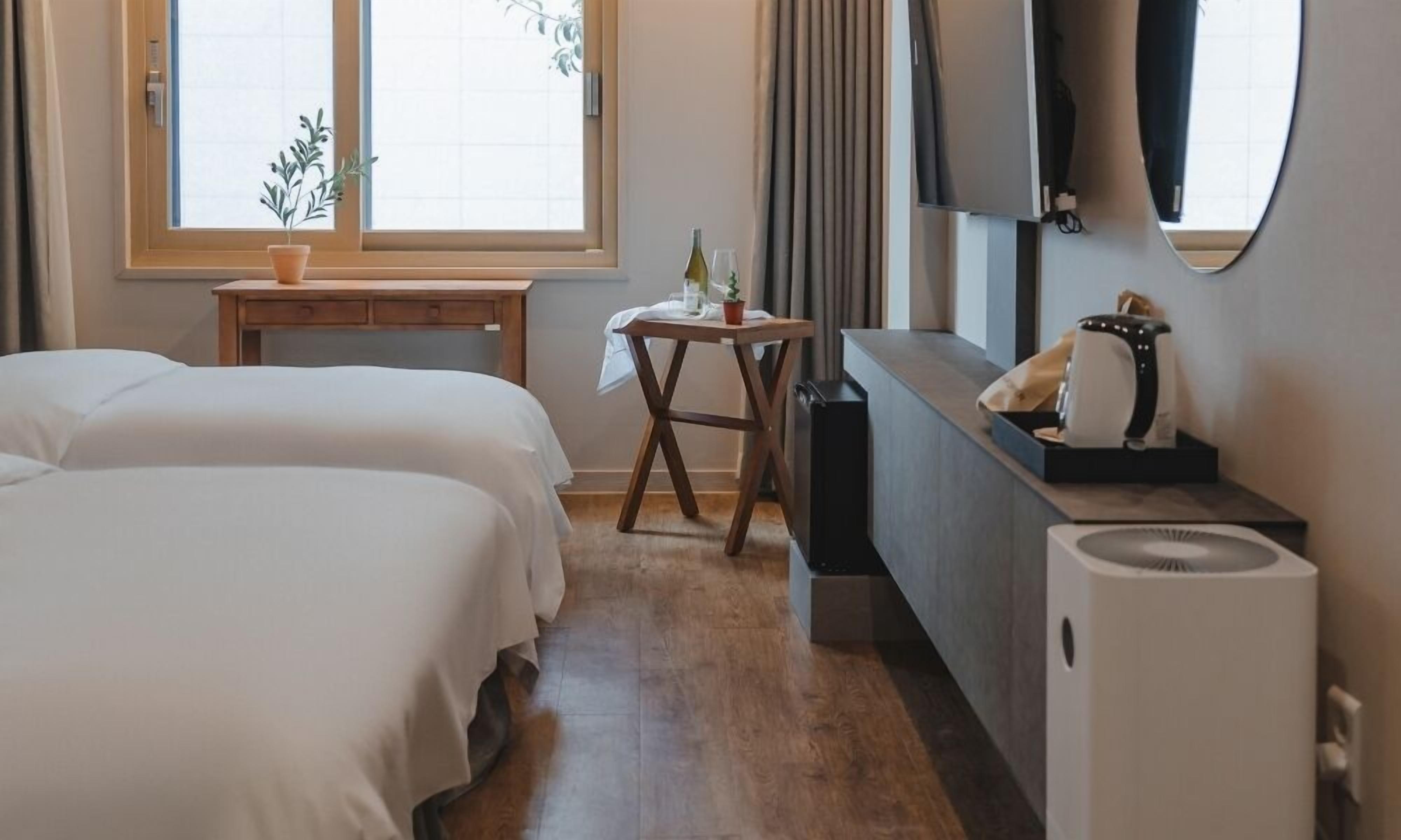 A hotel room with two beds, a small table with a plant, a desk with a computer, and a large mirror.