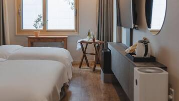 A hotel room with two beds, a small table with a plant, a desk with a computer, and a large mirror.
