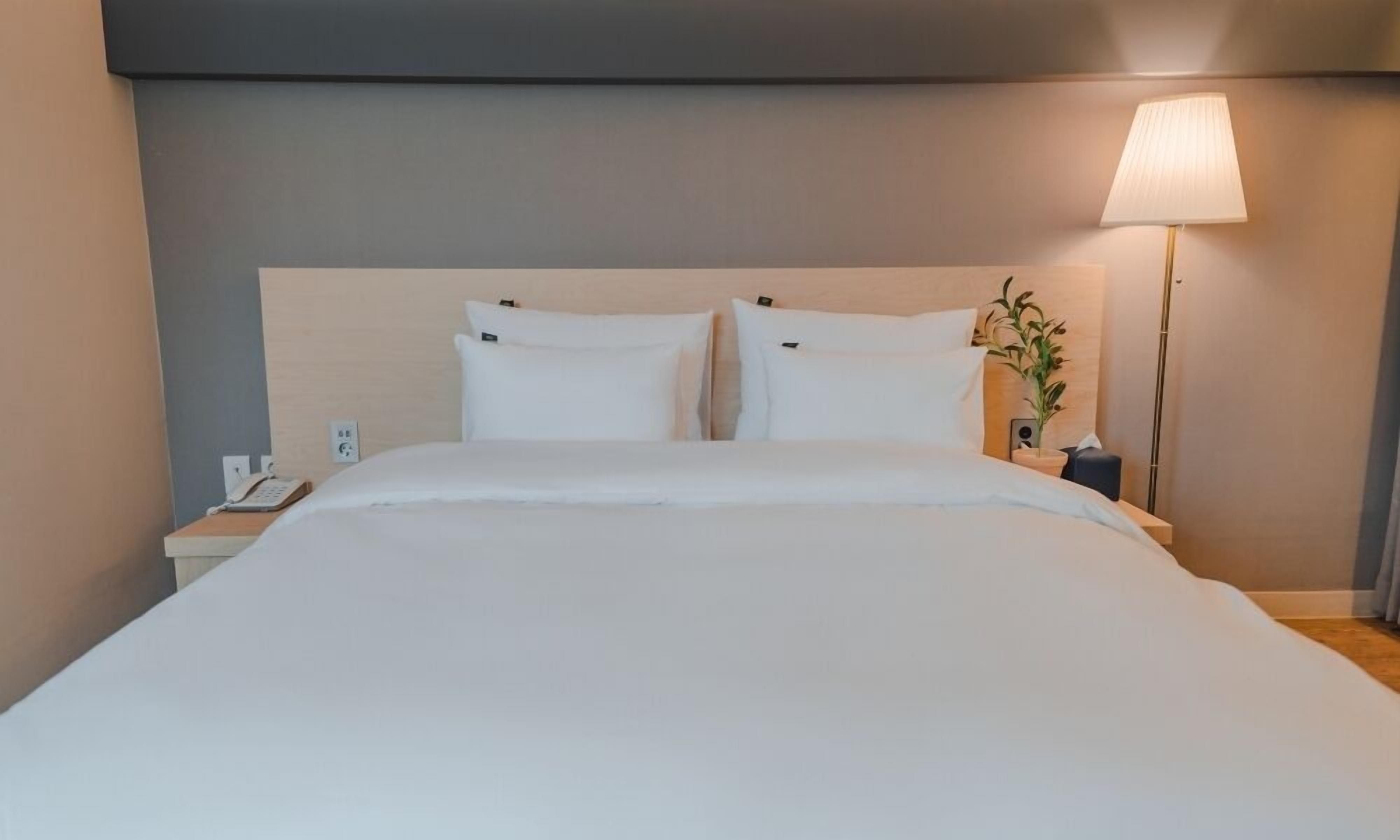 A neatly made bed with white linens, a bedside table with a lamp, and a phone on the nightstand.