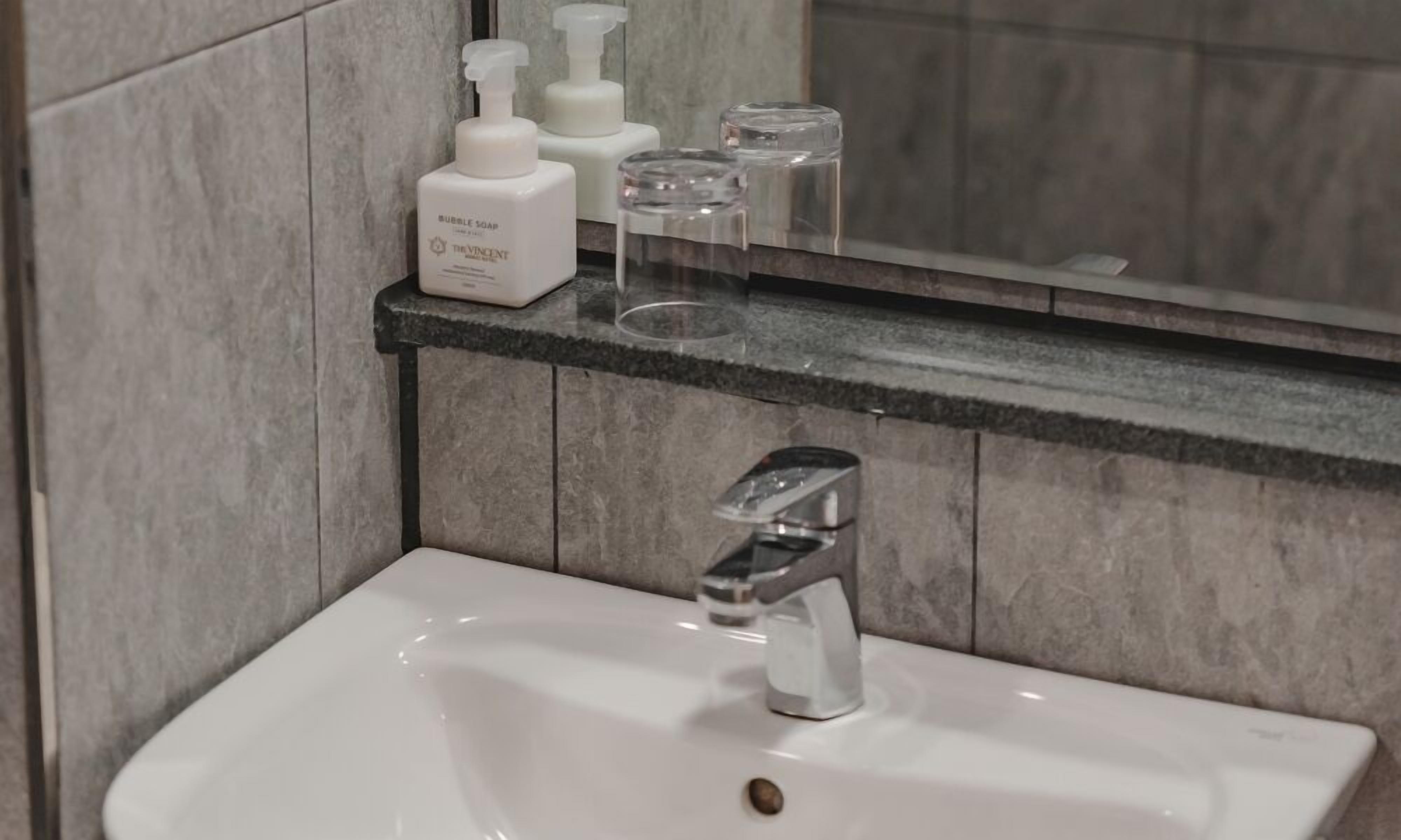 Un baño con lavamanos blanco, un espejo y artículos de aseo en un estante.