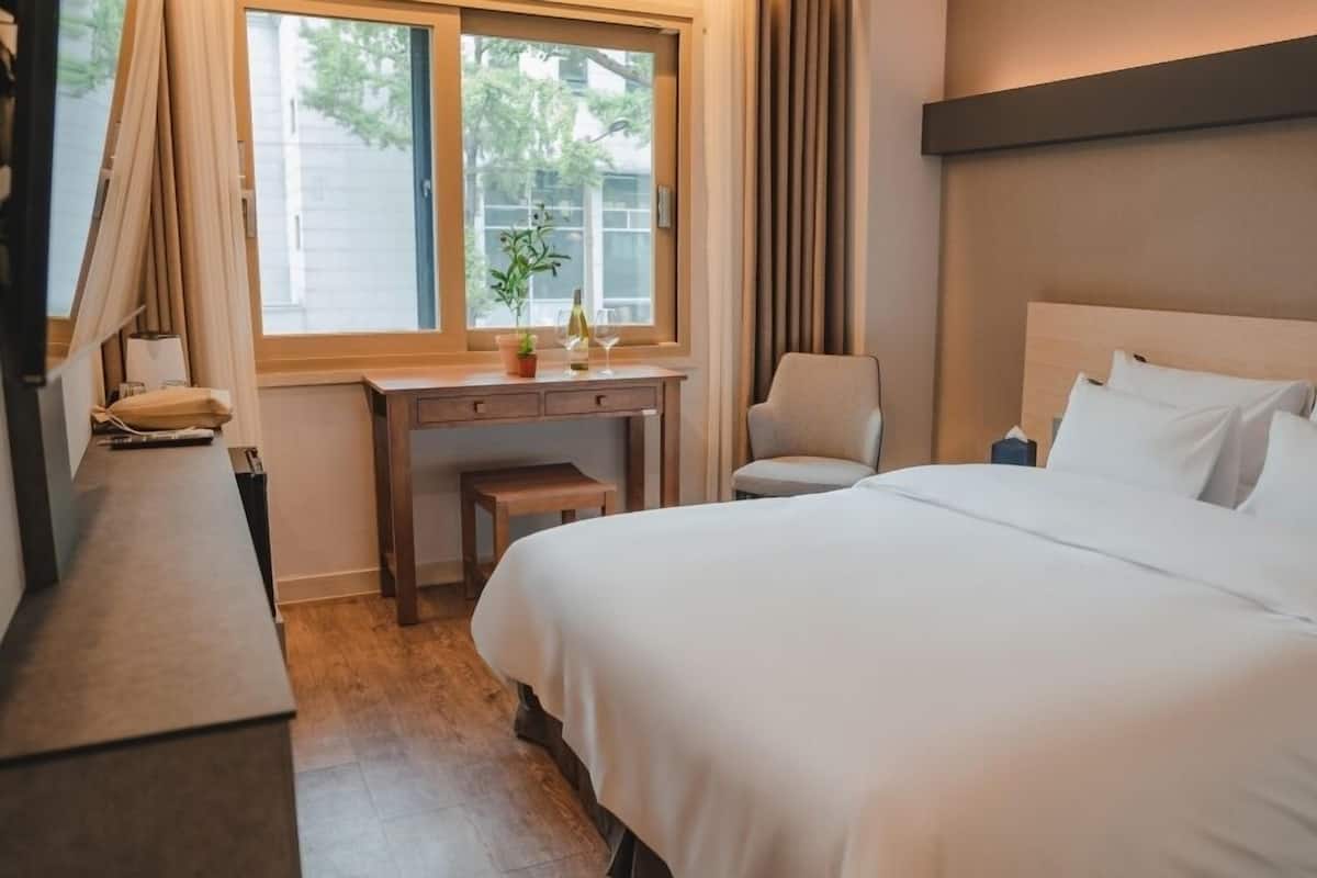Ein Hotelzimmer mit einem großen Bett, einem Schreibtisch, einem Stuhl und einem Fenster mit Vorhängen.