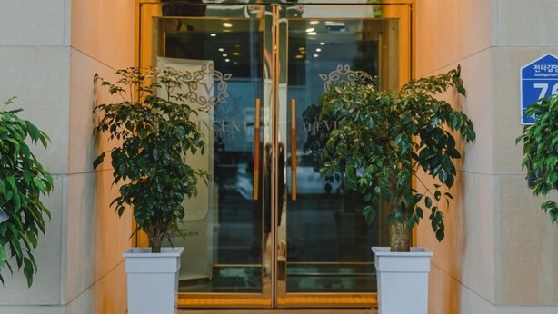 A hotel entrance with glass doors, potted plants, and a blue sign with Korean text. - Jeonju Hotel The Vincent (Jeonju)
