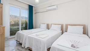 Et hotelværelse med to senge, et stort vindue med udsigt over landskabet og en aircondition-enhed på væggen.
