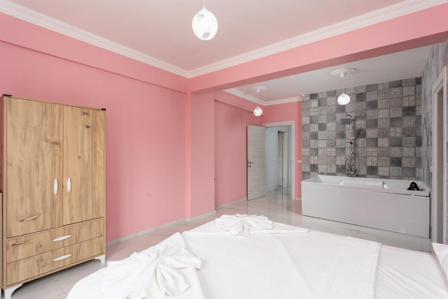 A bedroom with a large bed, a wooden wardrobe, and a bathroom with a tiled shower wall.