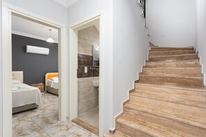 Un escalier menant à une salle de bain avec douche et un lit avec une table de chevet.