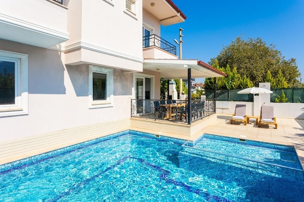 Une maison moderne à deux étages, dotée d’une piscine, d’un espace salon extérieur et d’un patio couvert.