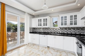 Una cocina moderna con armarios blancos, salpicadero a cuadros blanco y negro, y un ventanal con vistas a un patio.