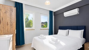 Quarto de hotel com cama, guarda-roupa, janela com cortinas, ar condicionado e vista para o verde lá fora.