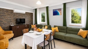 Uma sala de estar moderna com área de jantar, cortinas verdes, uma TV de tela plana e uma parede de pedra.