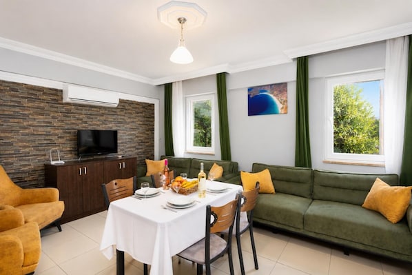 Una sala de estar moderna con comedor, cortinas verdes, un televisor de pantalla plana y una pared de piedra.