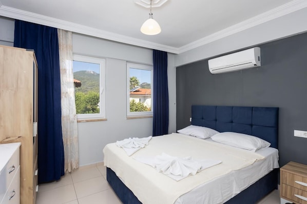A bedroom with a bed, a window, an air conditioning unit, and a wooden wardrobe.