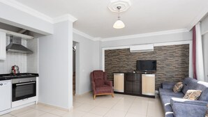 A modern living room with a grey sofa, a red armchair, and a TV mounted on a stone wall. - Villa Kaya 2 - Five Bedroom Villa, Sleeps 12 (Dalyan)