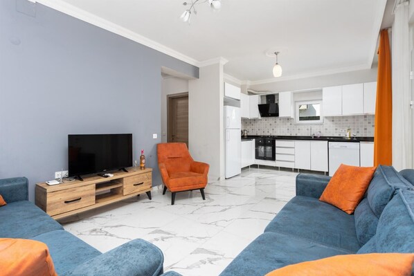 Een moderne woonkamer met een televisie, een oranje fauteuil en een blauwe bank.